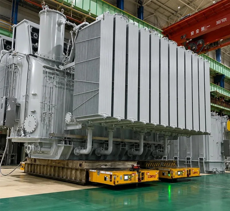 Dual 300-ton AGV automated guided vehicles transporting a 600-ton electrical transformer in a heavy equipment manufacturing plant