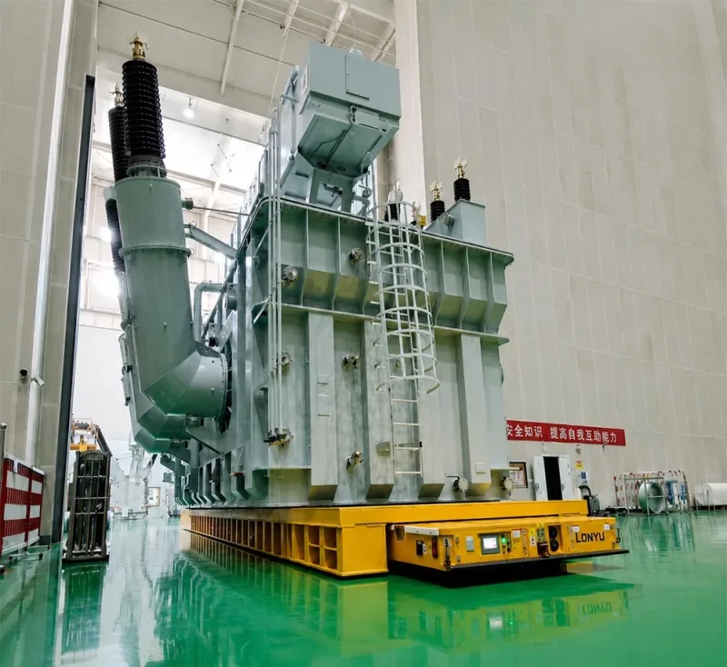 300-ton heavy-duty AGV transporting a UHV transformer inside a manufacturing plant with hydraulic suspension and omnidirectional steering system banner